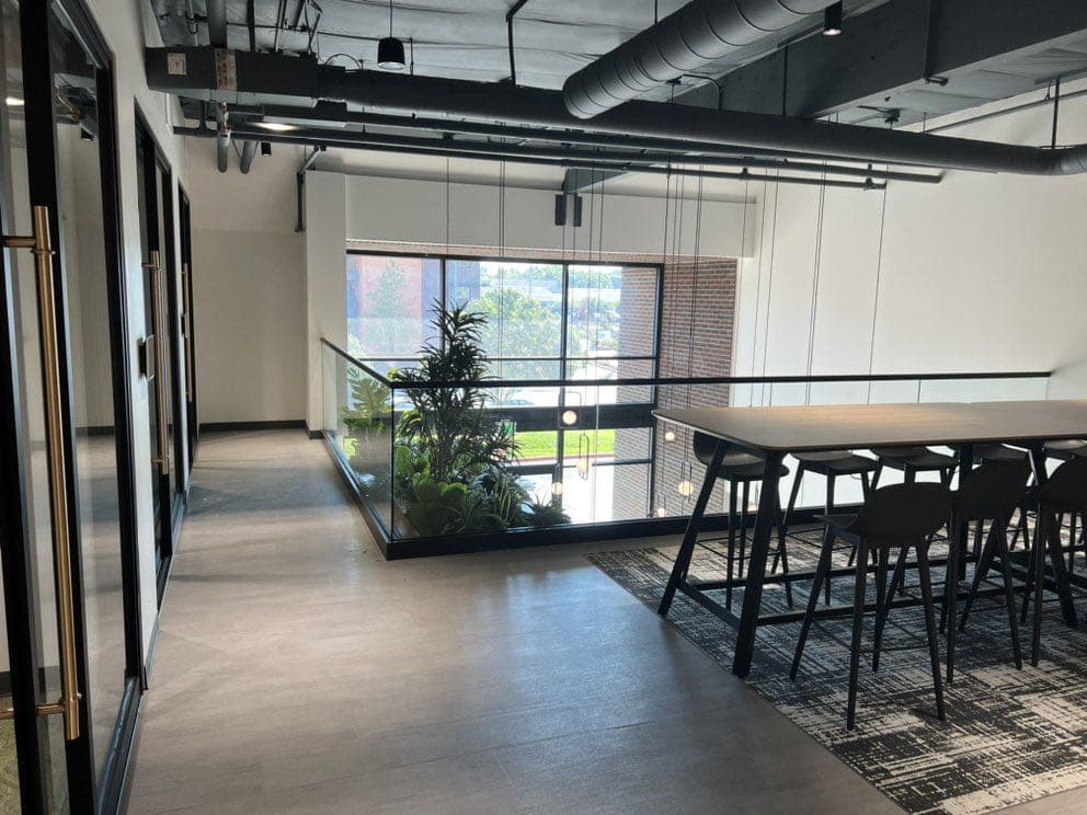 Office mezzanine edged with a frameless glass railing, overlooking a meeting table on the floor below