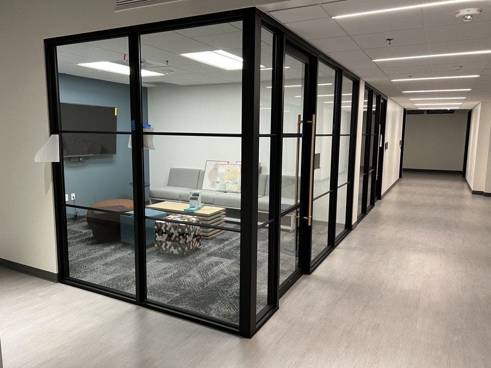 Black-framed glass office partitions with a glass door, lining a corridor in a finished commercial interior