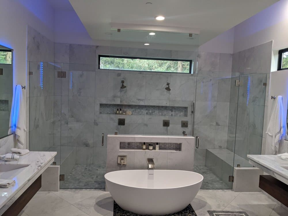 Large marble-tiled walk-in shower enclosed by frameless glass panels with a freestanding tub in front