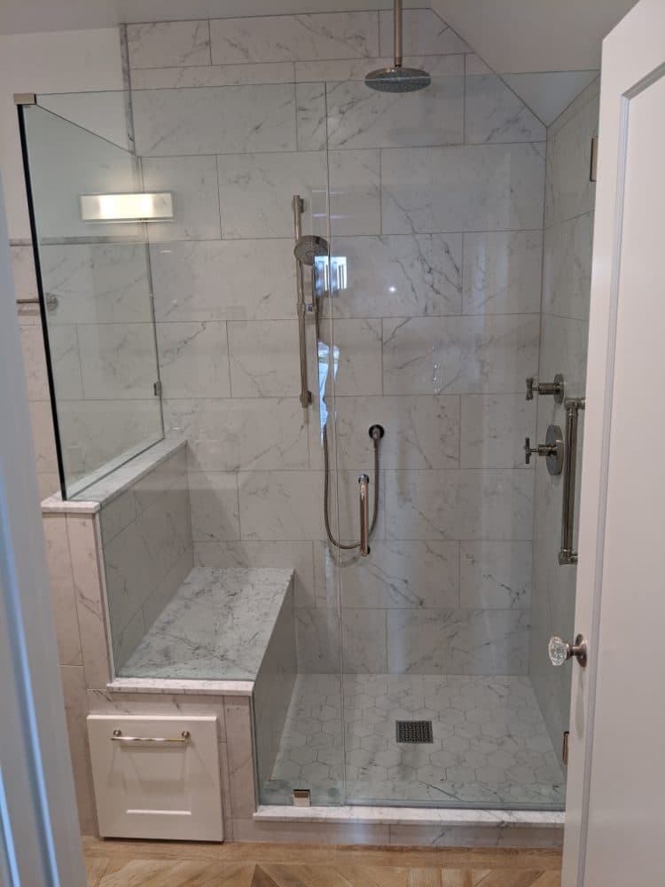 Frameless glass shower enclosure with a built-in marble bench and hinged door