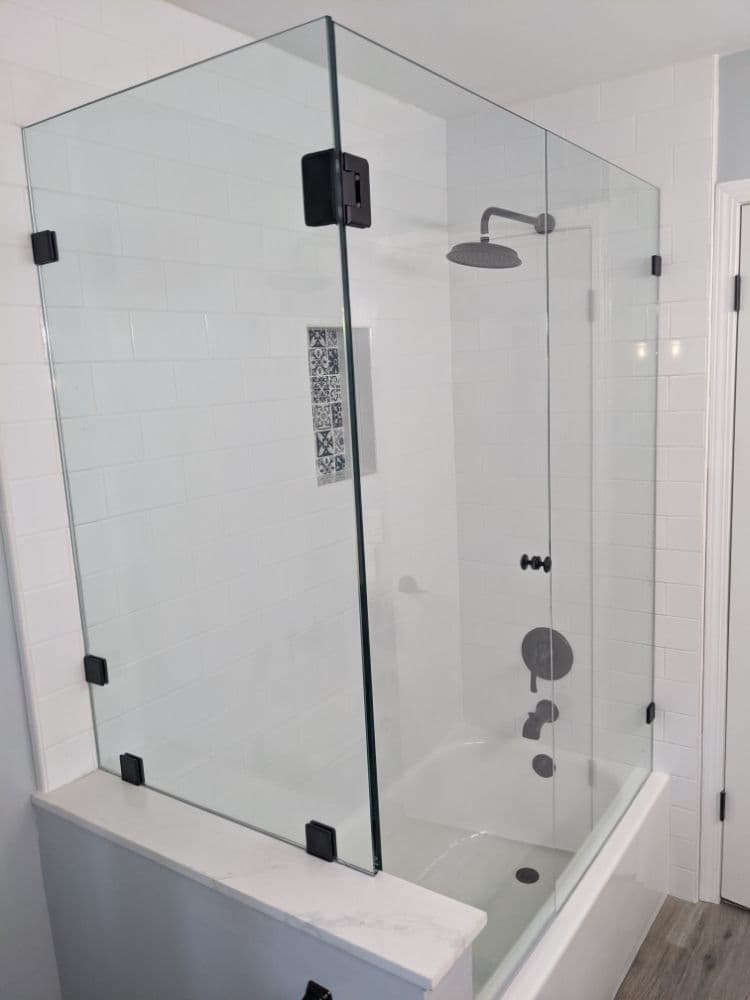Frameless glass tub screen with matte black clips enclosing a bathtub against white subway tile
