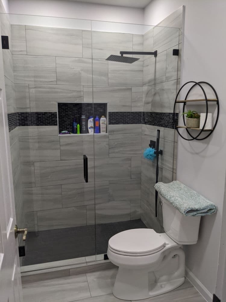 Newly tiled shower with a frameless glass door, matte black hardware and a recessed niche