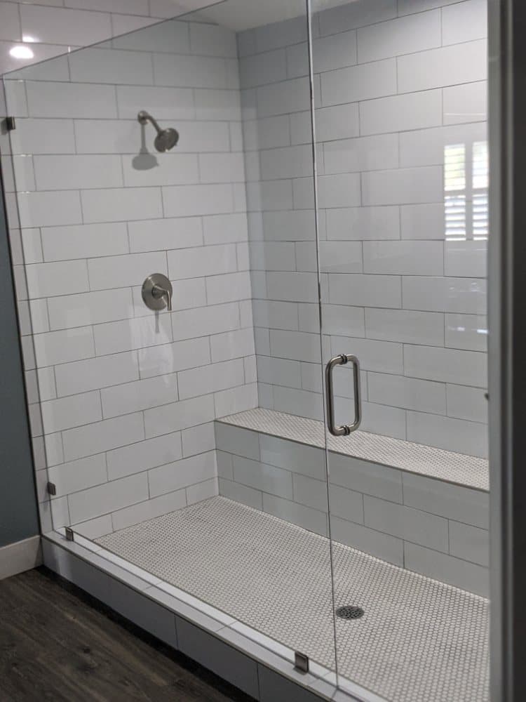 Frameless shower door and fixed panel enclosing a white subway tile shower with a built-in bench