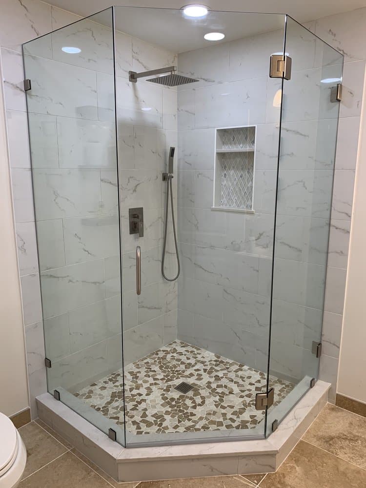 Neo-angle frameless shower enclosure with brushed nickel clamps and a marble-look tile surround